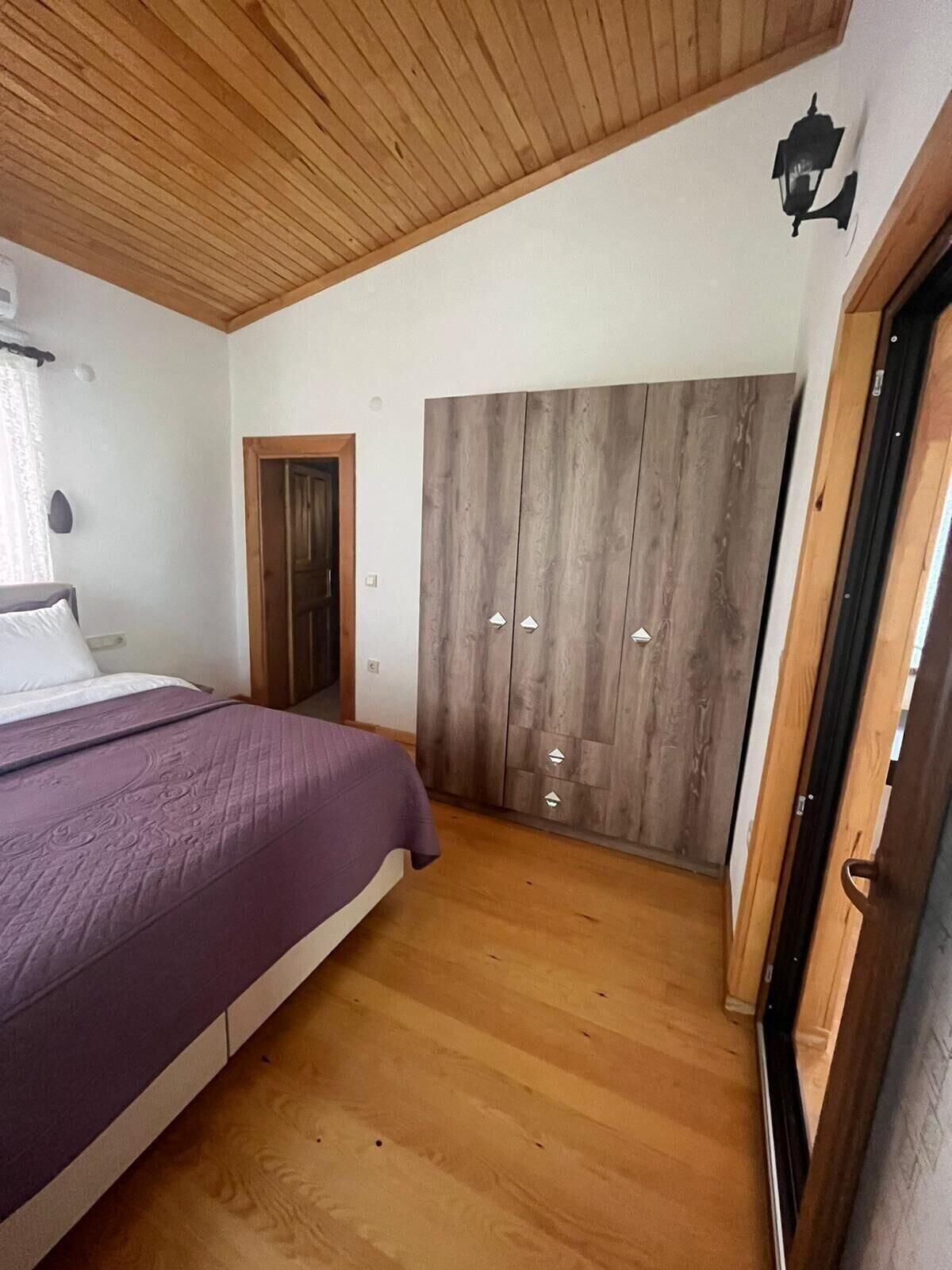A bedroom with a bed, wooden wardrobe, and a door.
