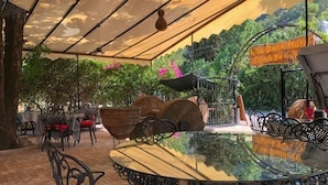 Un café en plein air avec des tables et des chaises rondes, entouré d’une végétation luxuriante et offrant une vue sur les montagnes.