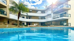 A modern hotel with a swimming pool, multiple balconies, and a palm tree. - ALVOR-ALGARVE SEASIDE  (Alvor)