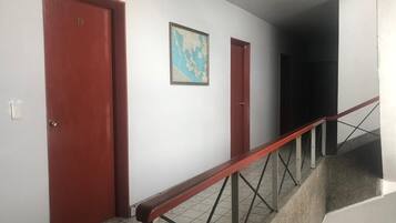 Um corredor com duas portas vermelhas, piso de azulejos e escada com corrimão de metal.