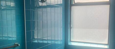 Un baño con azulejos azules, un inodoro blanco, un lavamanos con grifo y una ventana.
