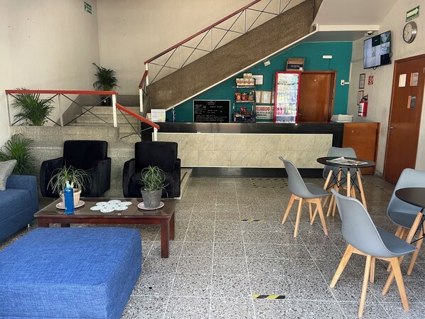 Un hall d’entrée comprenant un comptoir de réception, un espace salon, un escalier et un réfrigérateur.