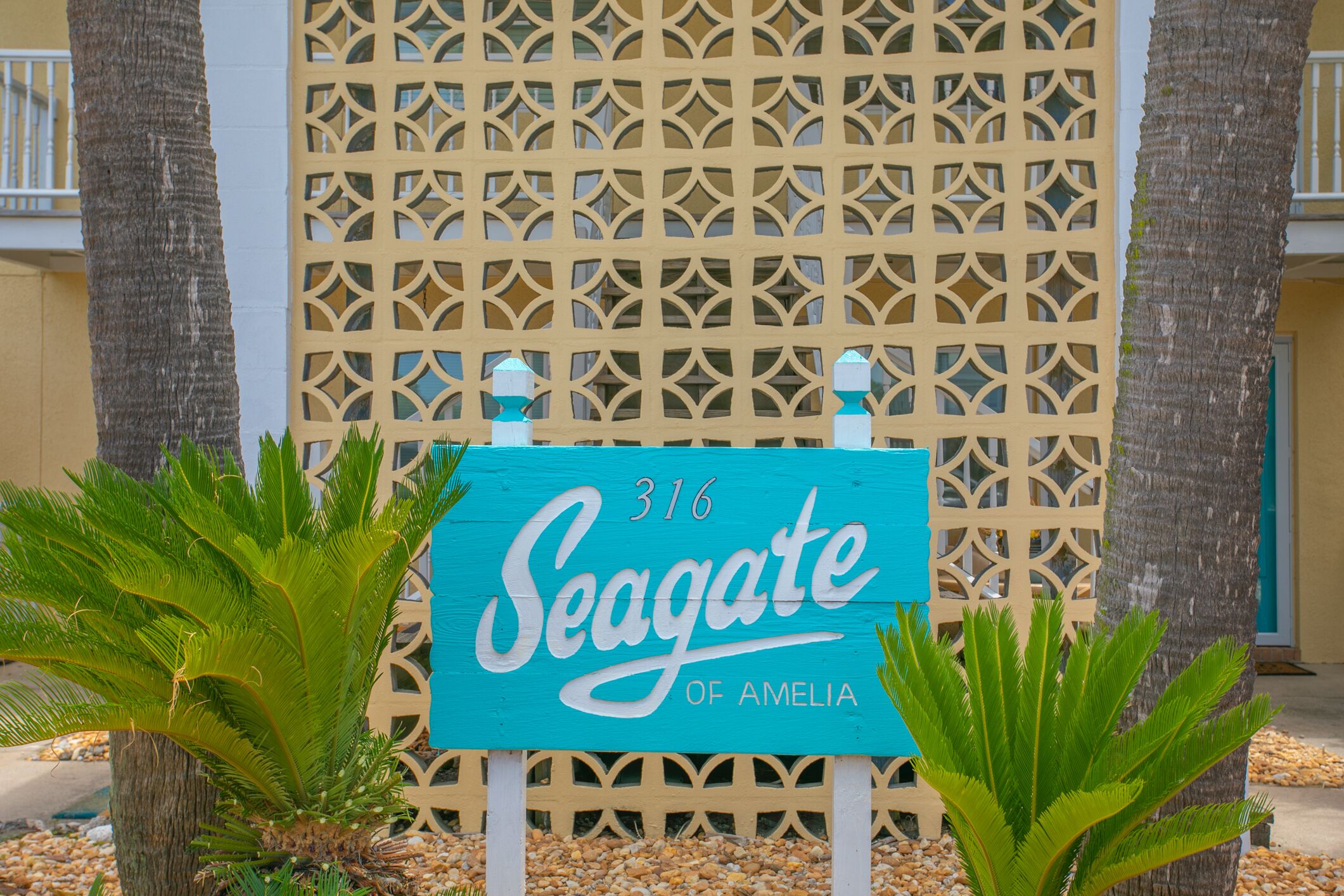 A sign for "Seagate of Amelia" with a decorative fence and palm trees in the foreground.