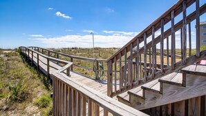 A wooden boardwalk extending over a grassy area with a clear sky. - Oceanfront | Spacious Deck | Beautiful Views | Seagate Condo (Fernandina Beach)