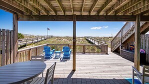 A wooden deck with a covered area, blue Adirondack chairs, and a table. - Oceanfront | Spacious Deck | Beautiful Views | Seagate Condo (Fernandina Beach)