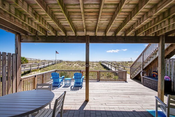 A wooden deck with a covered area, blue Adirondack chairs, and a table.