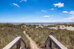 A wooden boardwalk leading to a beach with sand dunes and sparse vegetation.