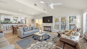 A spacious living area with a sofa, coffee table, and a dining table with chairs. A ceiling fan and a TV are visible.