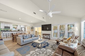 A spacious living area with a sofa, coffee table, and a dining table with chairs. A ceiling fan and a TV are visible.