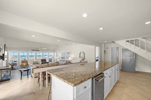 A spacious kitchen with a granite countertop, white cabinetry, and a stainless steel refrigerator.