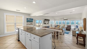 A spacious living area with a kitchen island, large windows, and a view of the beach.