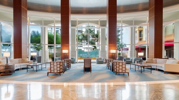 Eine großzügige Lobby mit Marmorboden, hohen Holzsäulen und einer Sitzecke mit Sofas und Sesseln.