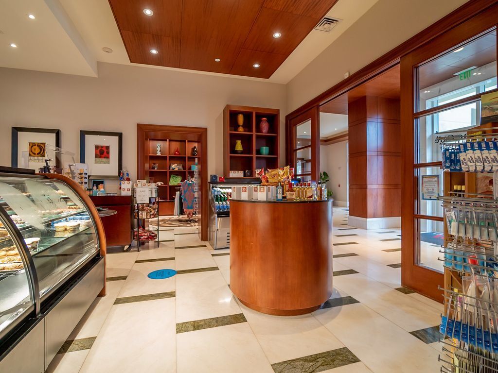 Un vestíbulo de hotel con un mostrador de recepción central, una vitrina de comida y una farmacia.