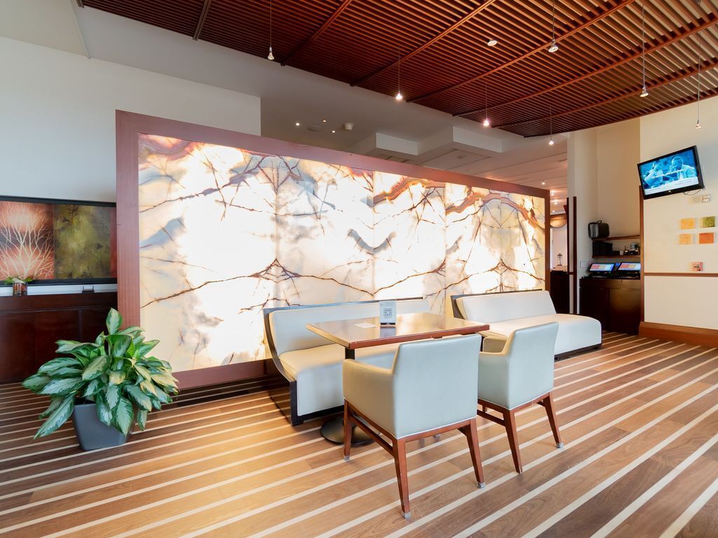 A modern hotel lobby with a marble wall, seating area, and a television.