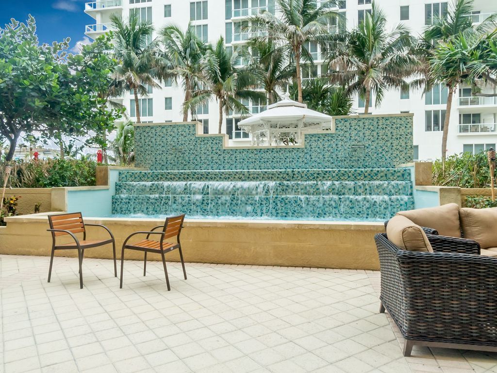 A pool area with a water feature, two chairs, and a wicker sofa.