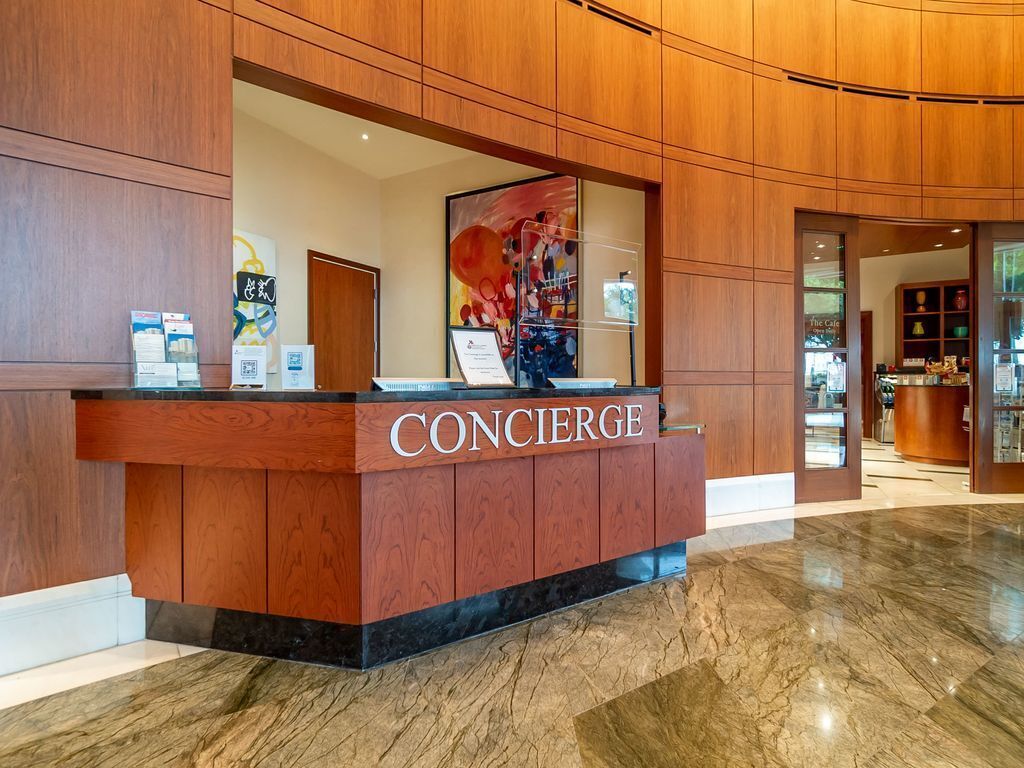 A wooden reception desk with the word "CONCIERGE" on it, surrounded by a polished marble floor and wooden paneling.