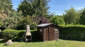 Un pequeño cobertizo de madera con chimenea de piedra, rodeado por un césped cuidado y abundante follaje.