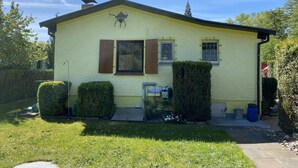 Una casa amarilla con dos ventanas, una chimenea y un pequeño jardín delantero con seto y camino pavimentado.