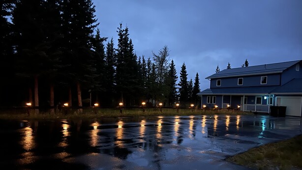 A residential area with a house, trees, and a wet ground reflecting lights.