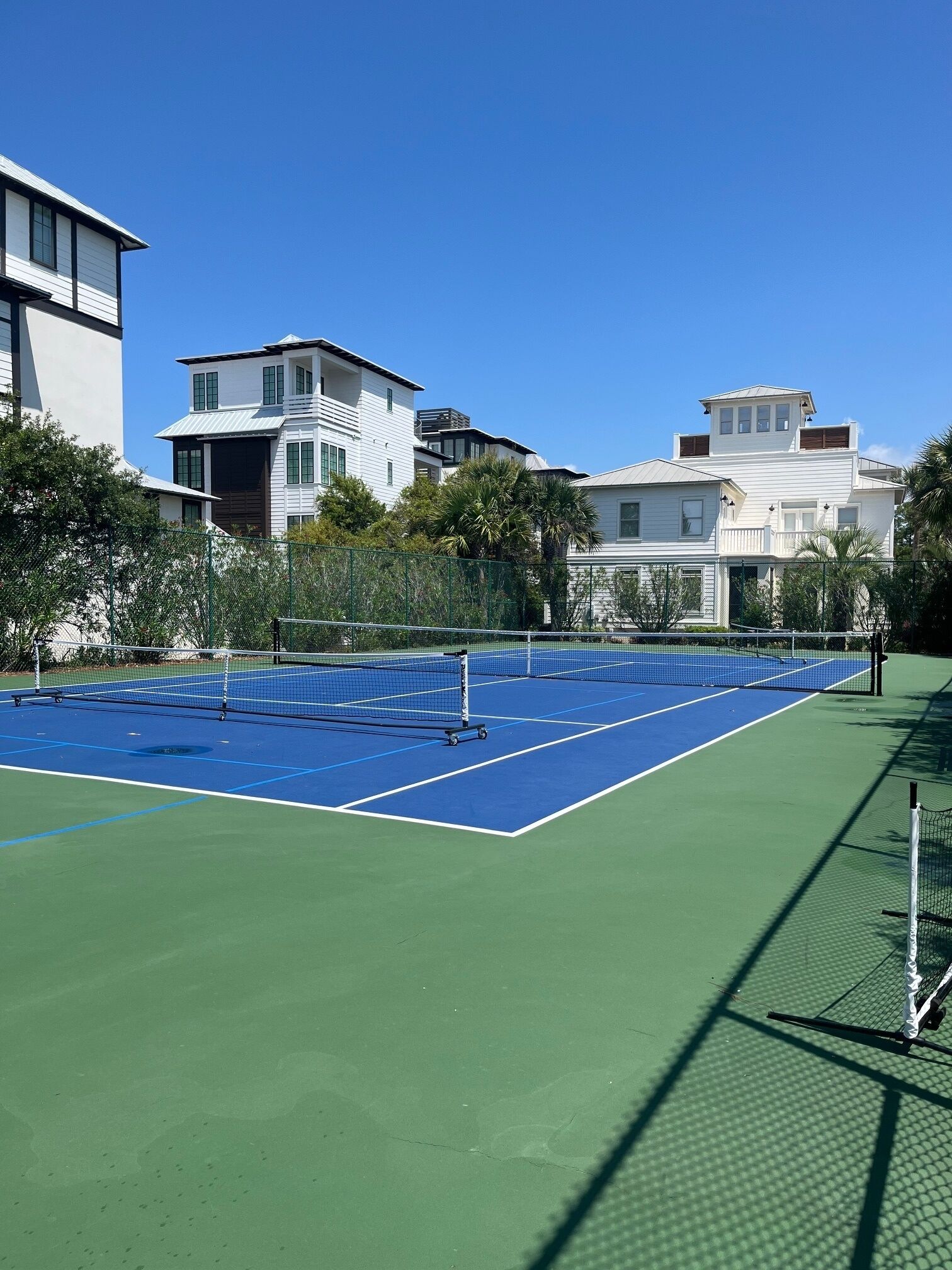 Un court de tennis avec un filet, entouré d’une clôture verte et d’arbres.