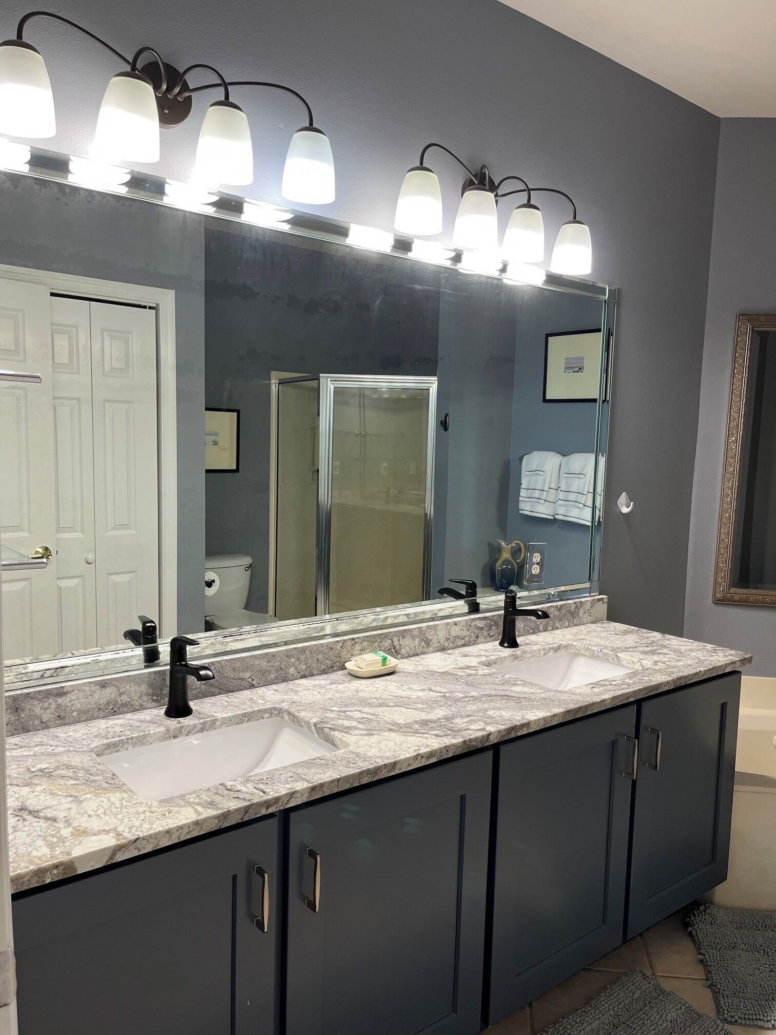 A bathroom with a double sink, a large mirror, and a wall-mounted light fixture.