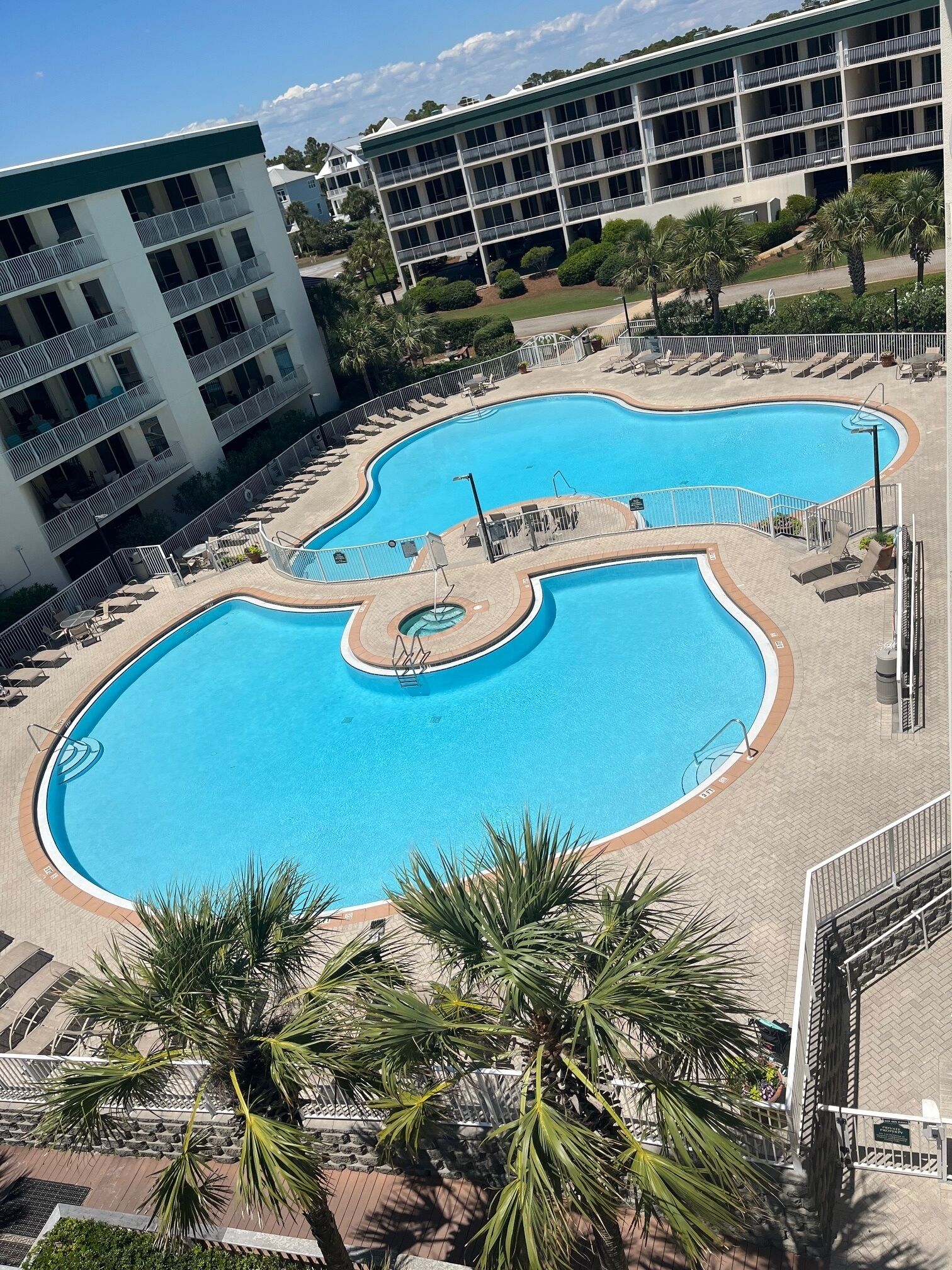 Een groot hotel met meerdere verdiepingen, een centraal gelegen zwembad, diverse balkons en palmbomen.