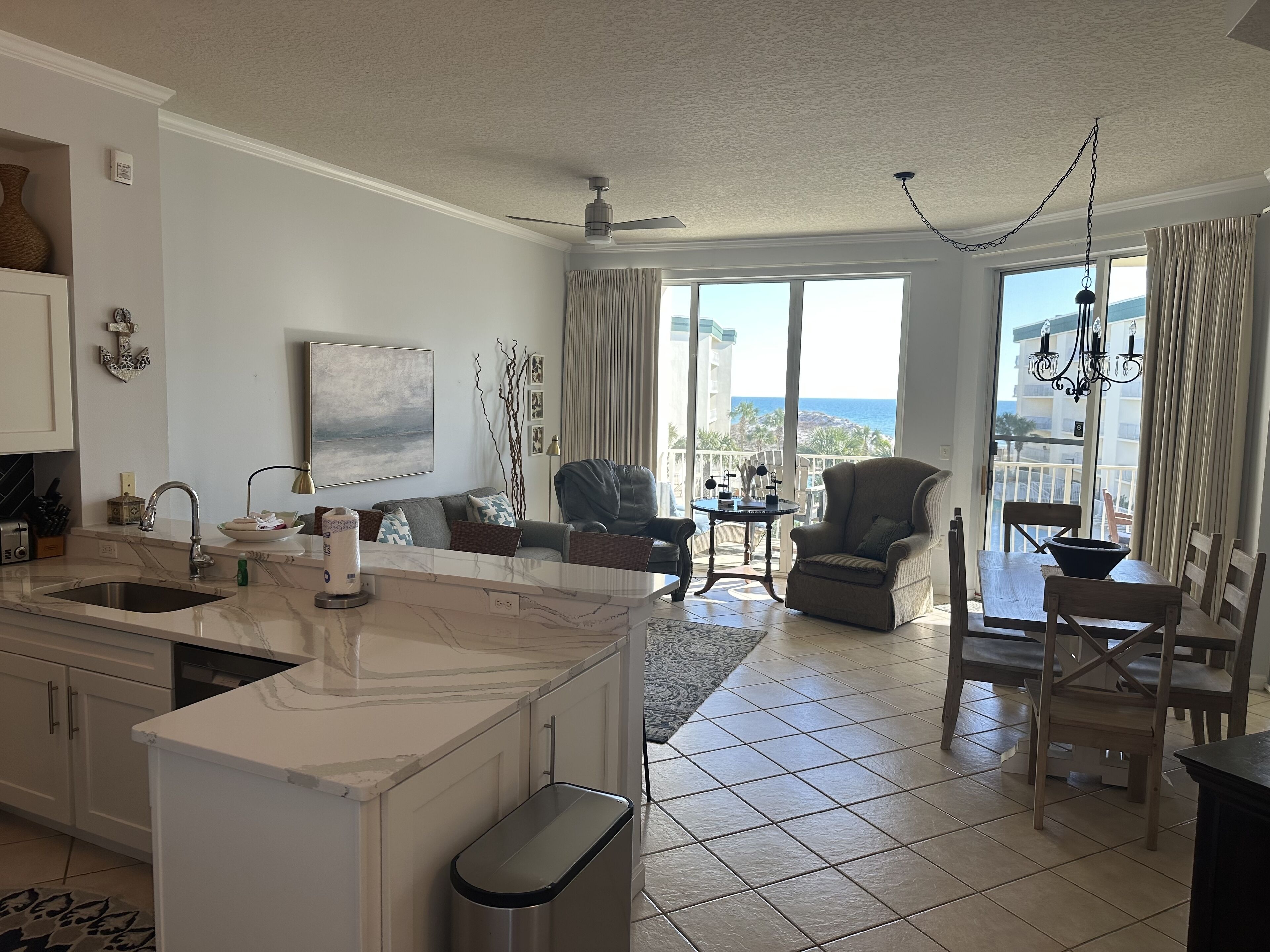 A modern living room with a kitchen, large windows, and a balcony with a view of the sea.