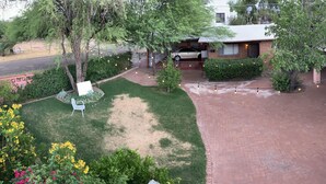 Un jardin arrière aménagé avec une terrasse dallée, un espace barbecue et une voiture garée dans l’allée.