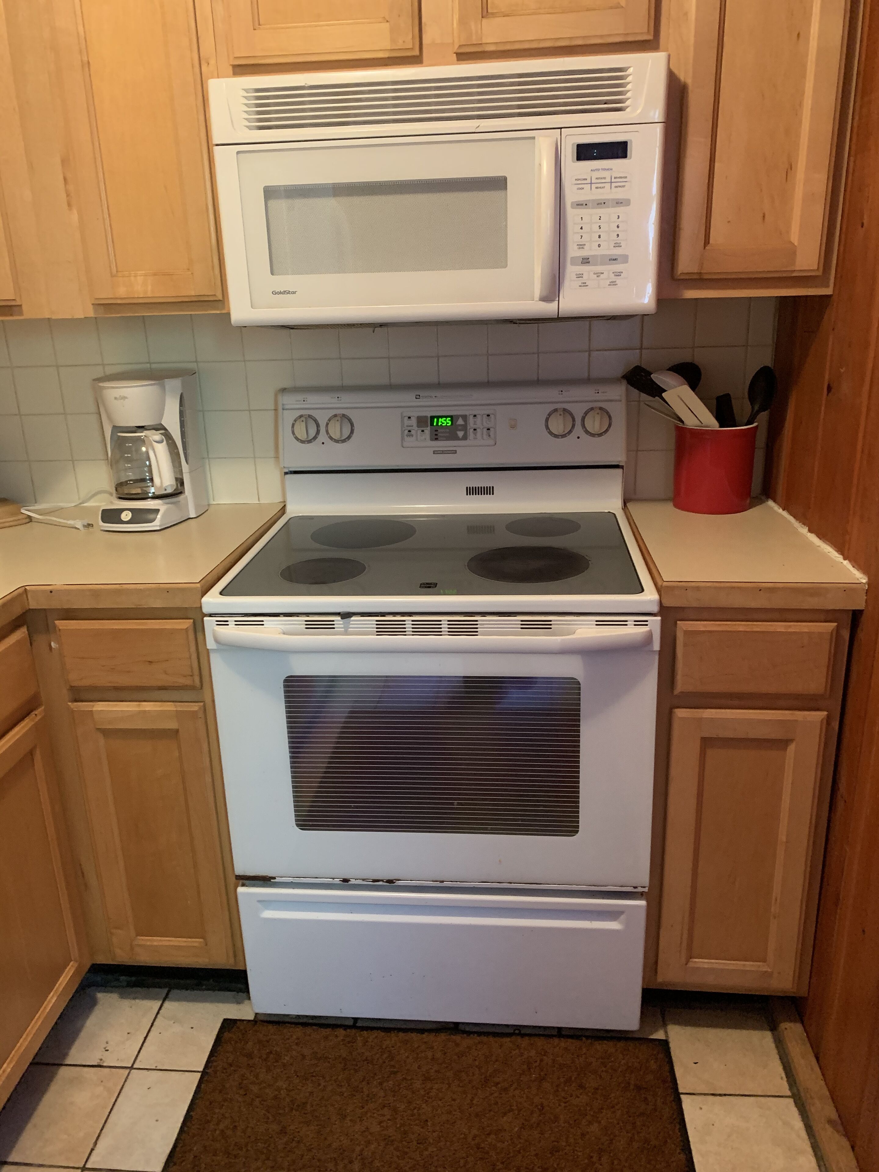 Una cocina con estufa blanca, microondas y cafetera.