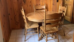Una mesa de madera para comer con seis sillas, un piso de baldosas y una puerta de madera al fondo.