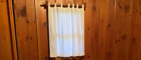 A room with wooden walls, a bed with a plaid bedspread, and a white curtain.