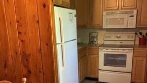Una cocina con armarios de madera, un refrigerador, un microondas, una estufa y una cafetera.