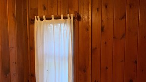 Una habitación con paredes de madera, una cama blanca con colcha y una cortina blanca sobre una ventana.