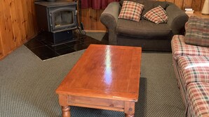 Un salón acogedor con interior de madera, un sofá con cojines escoceses, una mesa de centro de madera y un estufa de leña.