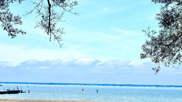 Una playa con una mesa de picnic y sillas, un faro a lo lejos y un mar tranquilo.
