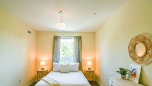 A bedroom with a large bed, two bedside lamps, a bedside table with a lamp, a dresser, a window with curtains, and a wall-mounted mirror. - Greensview Apartment | 2 Bedroom, 2 Bath - Beautiful views! (Charlottesville)