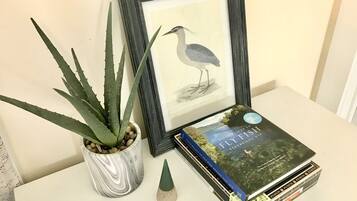 A framed bird illustration, a potted aloe plant, a book titled 'Fifty Places to Fly Fish Before You Die', and a small conical object on a white surface.