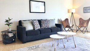 A modern living room with a dark sofa, patterned cushions, a small round table, and two folding chairs. - Greensview Apartment | 2 Bedroom, 2 Bath - Beautiful views! (Charlottesville)