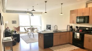 A modern kitchen with a central island, a dining area with chairs, and a large window providing natural light. - Greensview Apartment | 2 Bedroom, 2 Bath - Beautiful views! (Charlottesville)