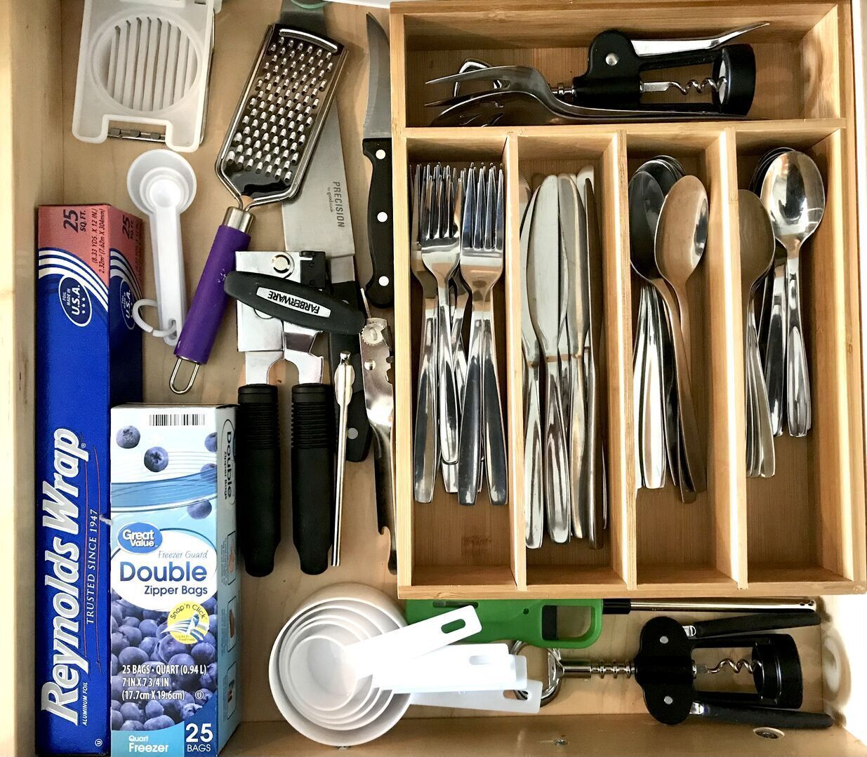 Un tiroir contenant divers ustensiles de cuisine, notamment une râpe, un ouvre-boîte, ainsi que plusieurs cuillères et fourchettes.