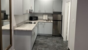 A compact kitchen with white cabinets, a stainless steel refrigerator, a microwave, and a granite countertop. - Palace Inn Crosby (Crosby)
