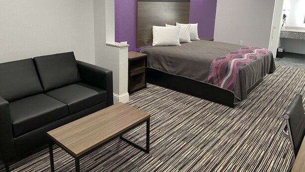 A modern hotel room with a bed, a black sofa, a wooden coffee table, and a patterned carpet. - Palace Inn Crosby (Crosby)