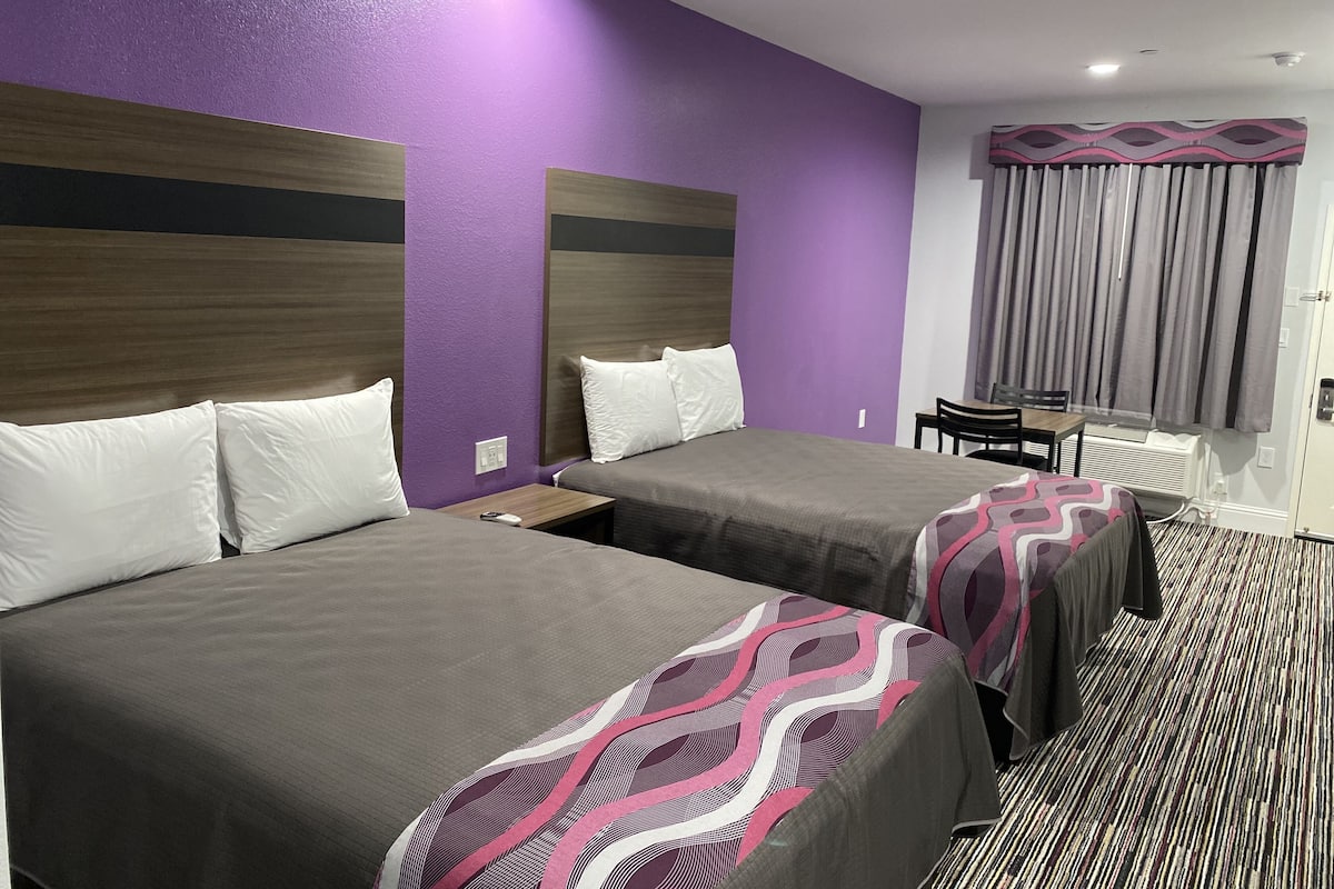 A hotel room with two beds, a desk, and a window with curtains.