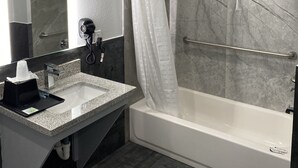 A modern bathroom with a marble shower, a glass-enclosed bathtub, a vanity with a sink, and a hairdryer on the wall. - Palace Inn Crosby (Crosby)