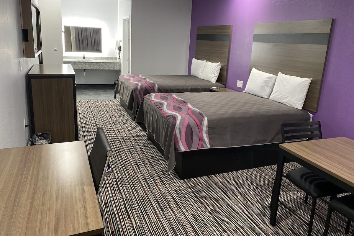 A hotel room with two beds, a desk, a chair, a small table, and a mirror.