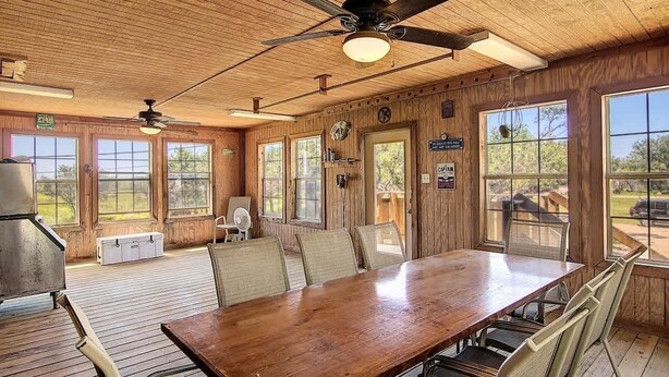Un intérieur en bois avec une grande table à manger, des ventilateurs de plafond et de grandes fenêtres.