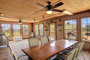 Ein Holzinterieur mit einem großen Esstisch, Deckenventilatoren und großen Fenstern.