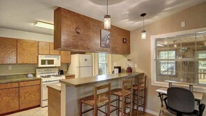 Une cuisine avec des meubles en bois, un îlot central doté de tabourets, un réfrigérateur, une cuisinière et des luminaires suspendus.