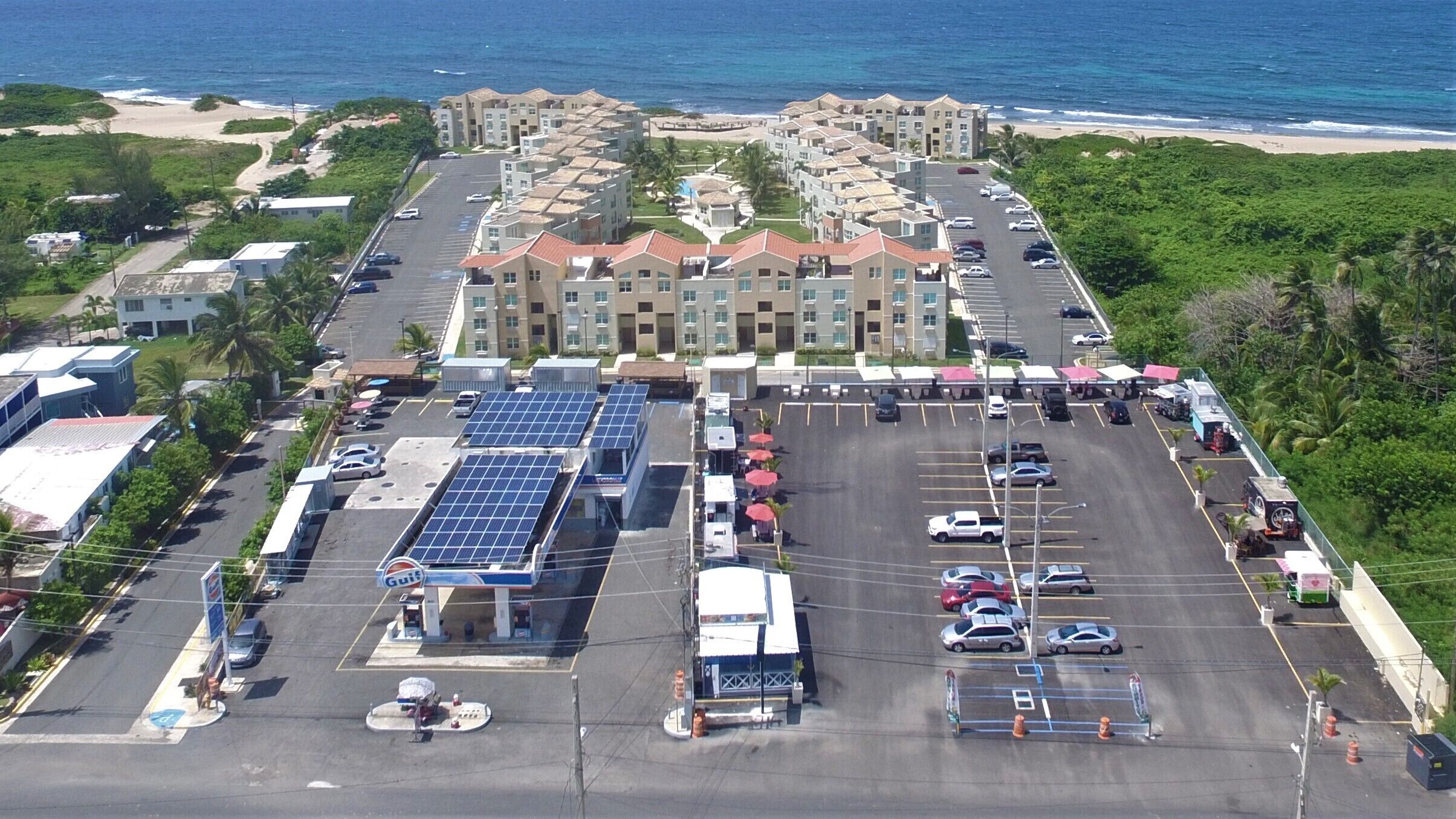 Un hotel de varios pisos con estacionamiento, paneles solares y vista al mar.