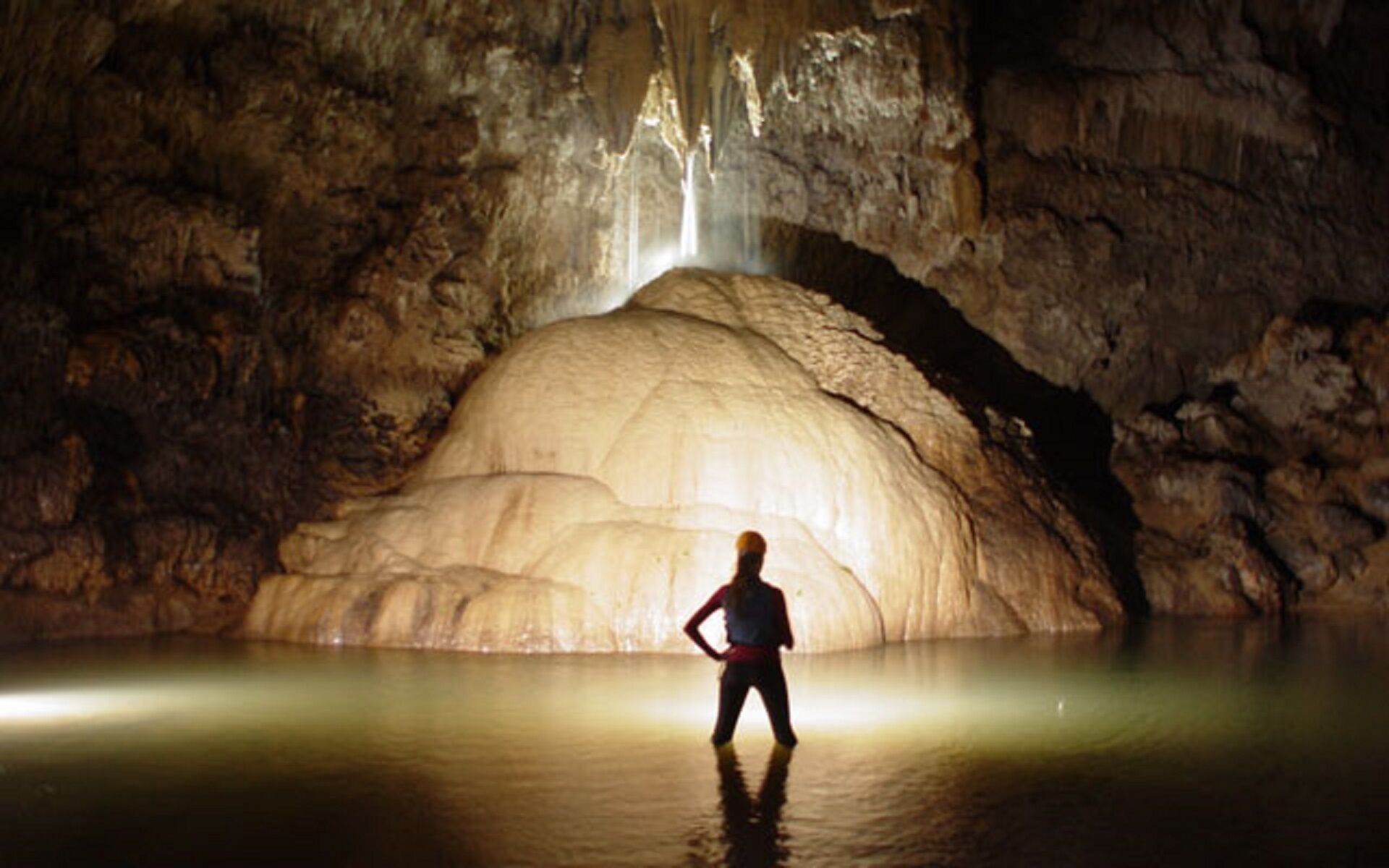 Une personne se tient dans une grotte, avec une grande formation rocheuse et une cascade en arrière-plan.